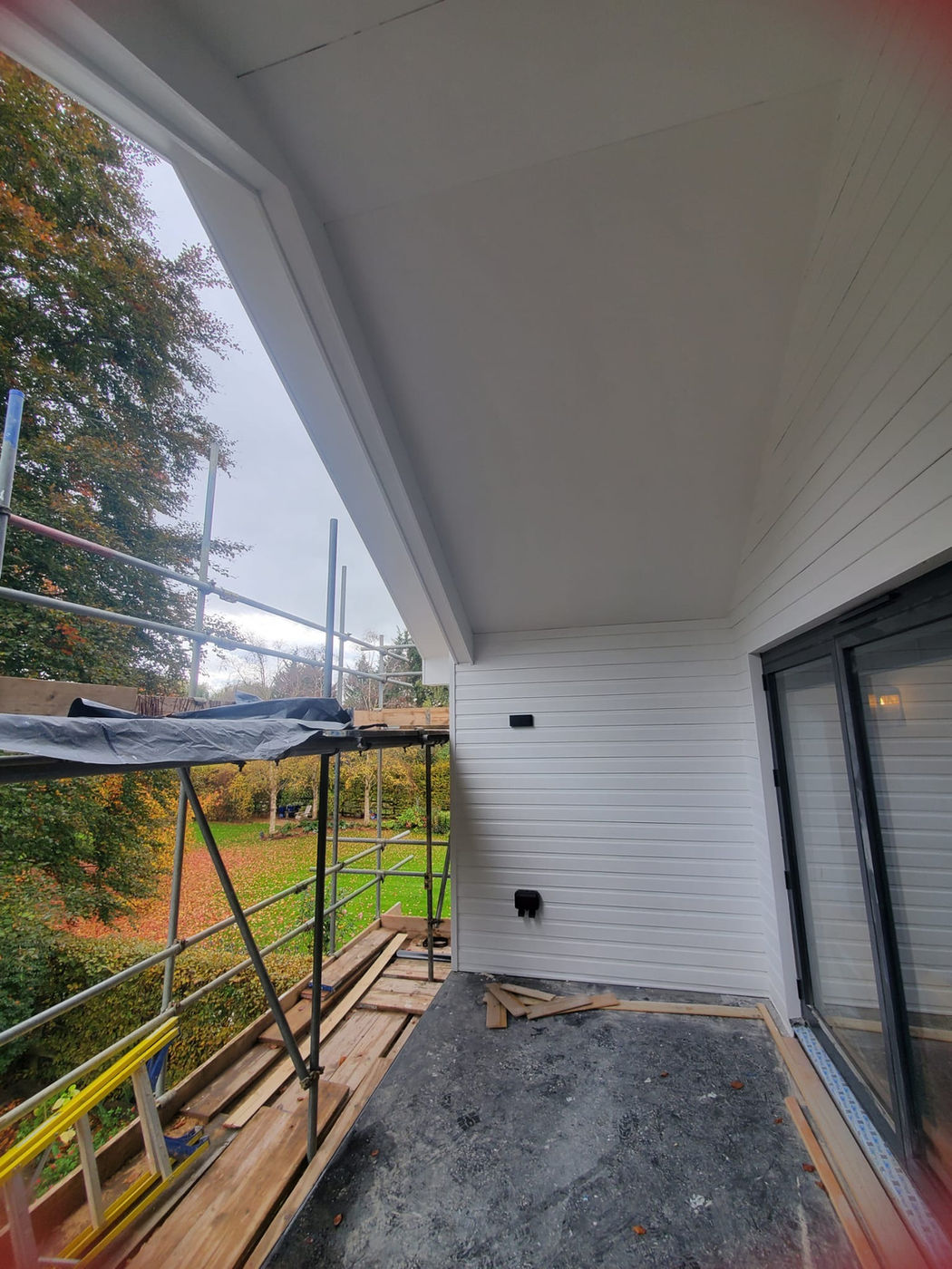 White exterior soffit and cladding detail beside scaffolding
