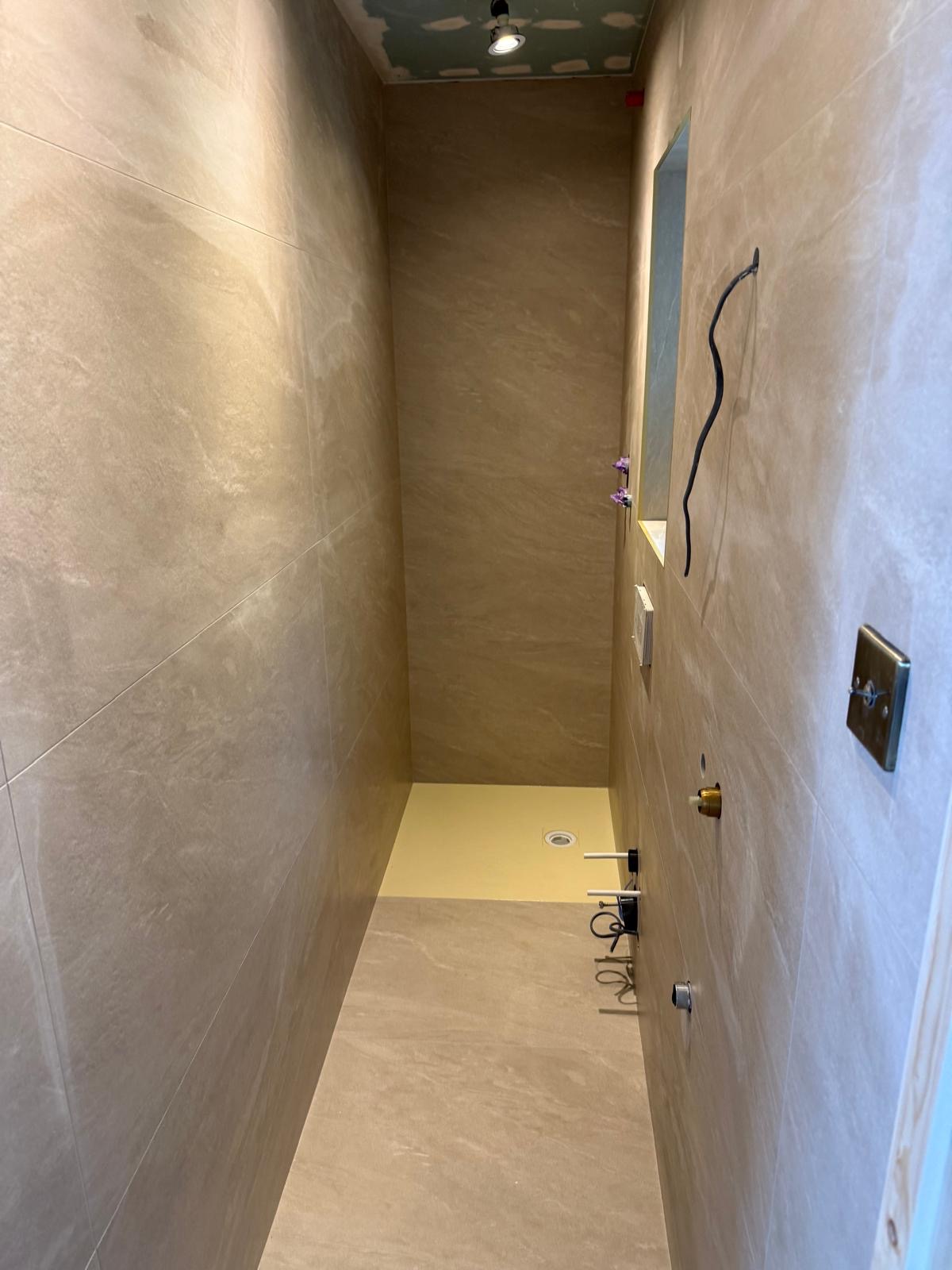 Walk in shower area with large wall tiles and shower tray preparation